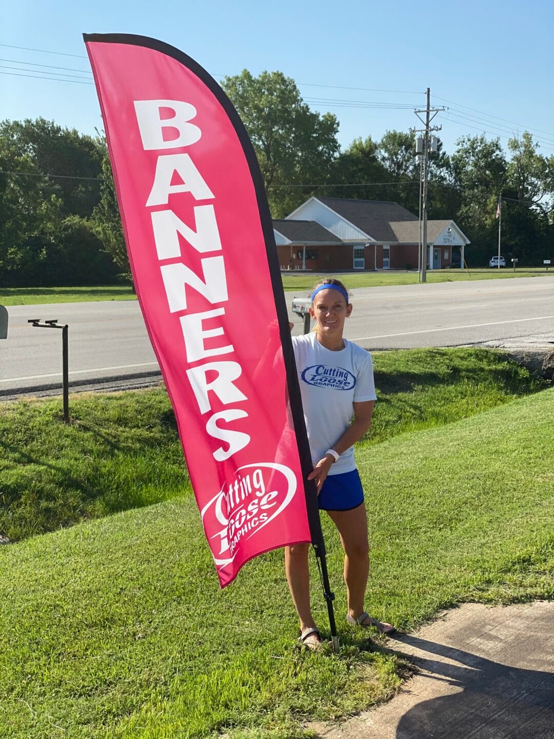Clarissay Hallacy of Cutting Loose Graphics standing next to a giant red Flag Banner by the road on North Main in Joplin, MO.