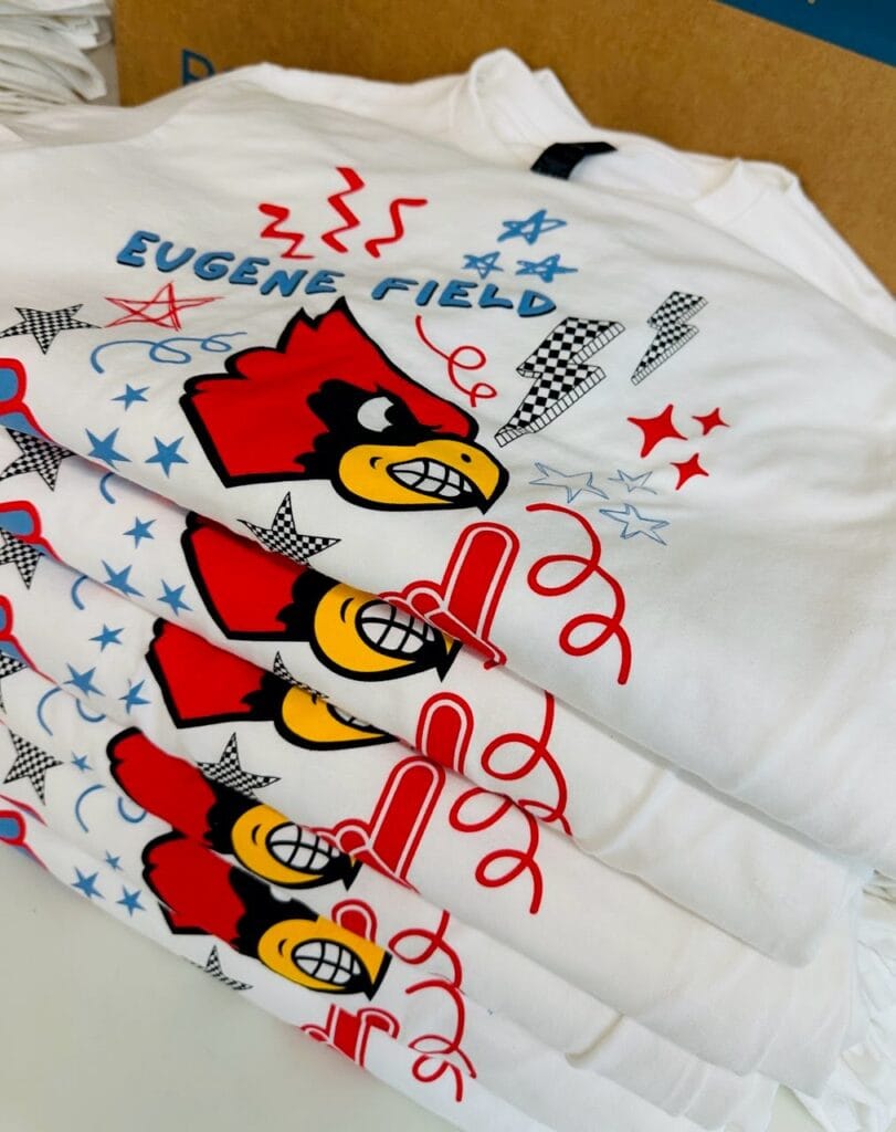 A stack of white custom screen printed shirts for Eugene Field Elementary in Webb City, MO that says "Let's Go Cards"
